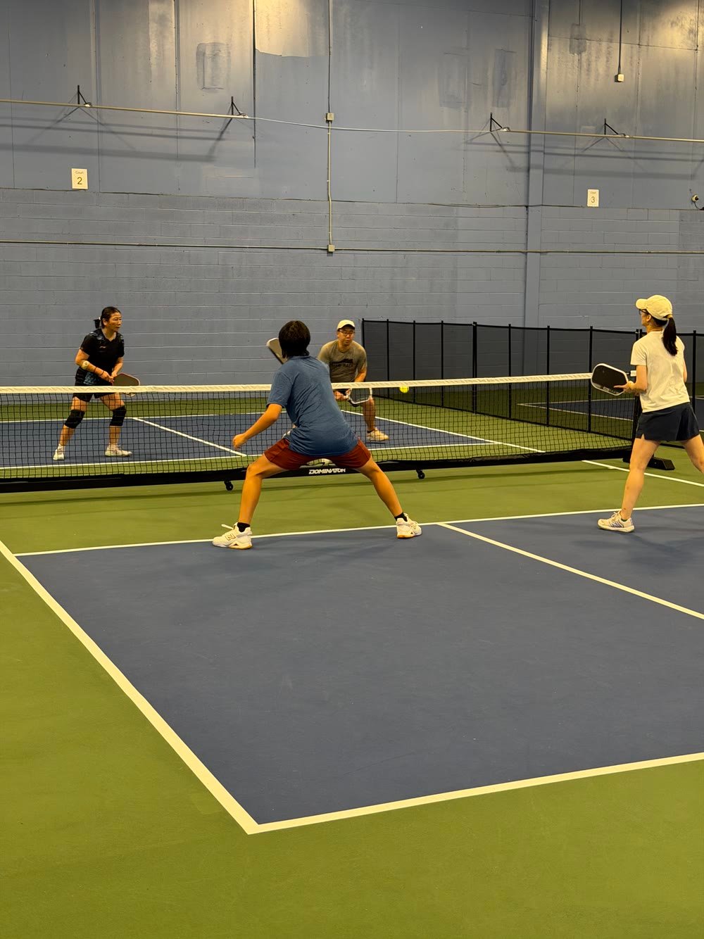 Four players in a doubles rally at the kitchen line