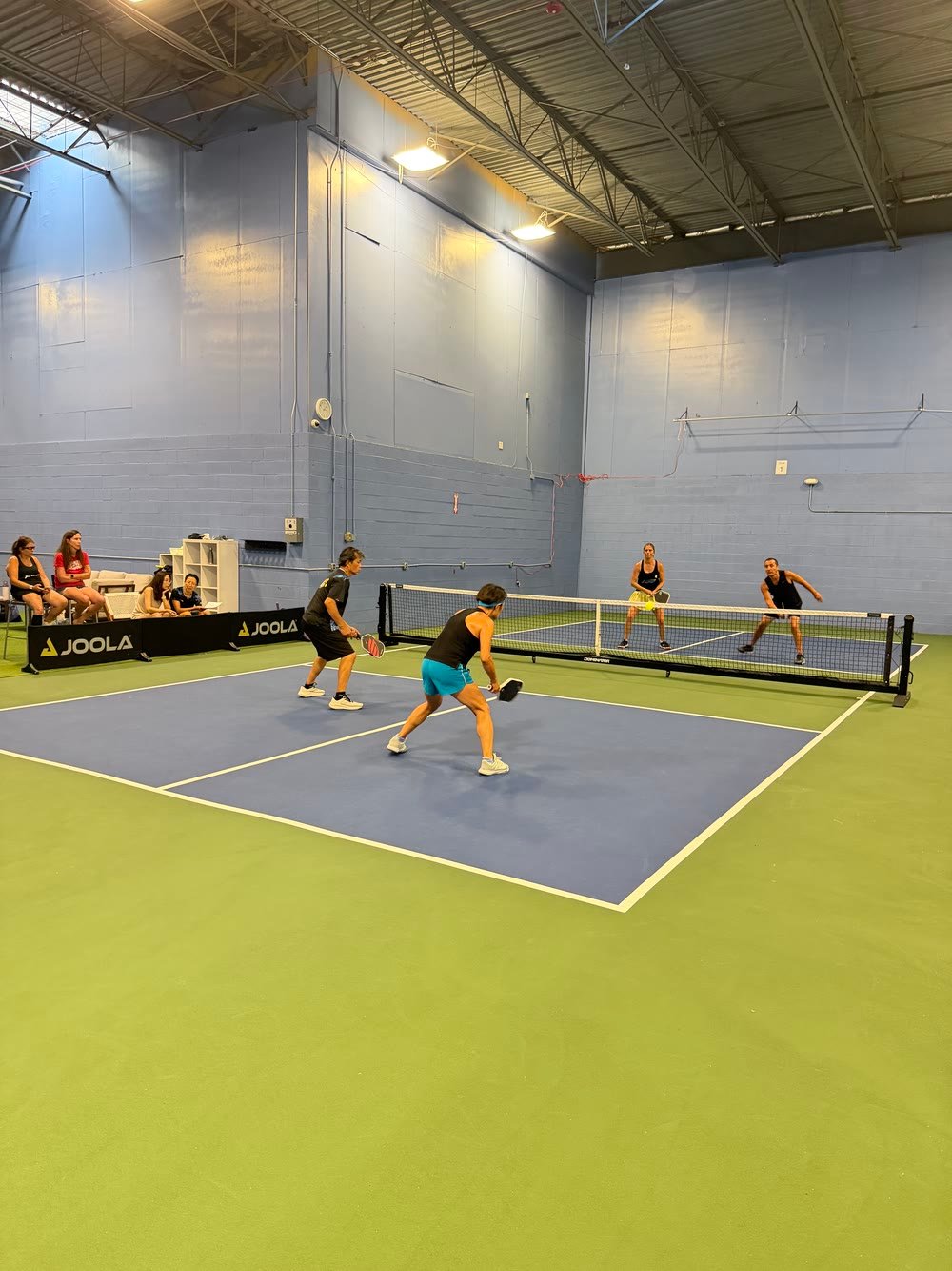 Doubles on a blue court while friends watch from the sideline